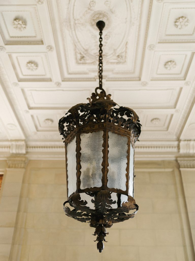 Exquisite Aldrich Mansion wedding interior detail highlighting an ornate vintage hanging lantern and a carved coffered ceiling
