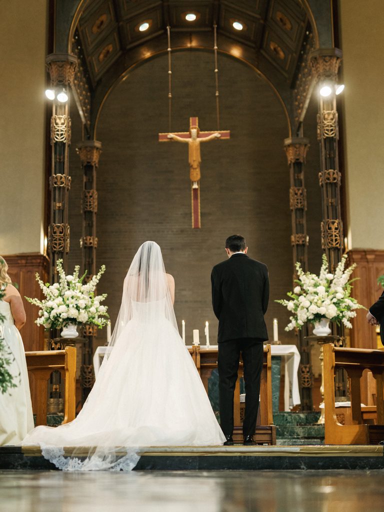 Traditional Aldrich Mansion wedding ceremony showcasing the bride and groom standing together at the grand wooden altar with a large cross