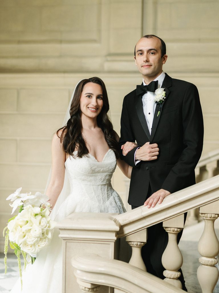 Stunning newlyweds portrait posing on a majestic marble staircase with a luxury white orchid wedding bouquet