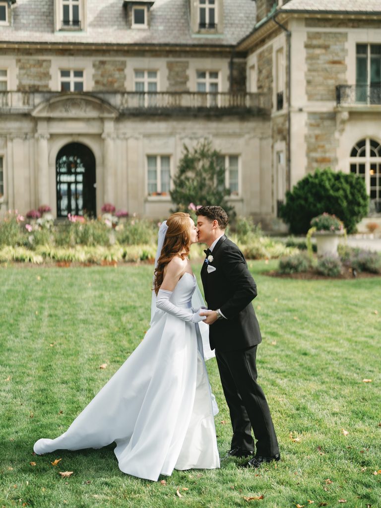 Luxury couple portrait showcasing a sweet embrace and kiss on a green lawn with a majestic chateau facade behind them