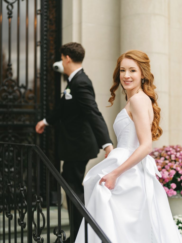 Captivating Aldrich Mansion wedding candid moment showing a beautiful red haired bride in a satin gown walking up the grand stone stairs