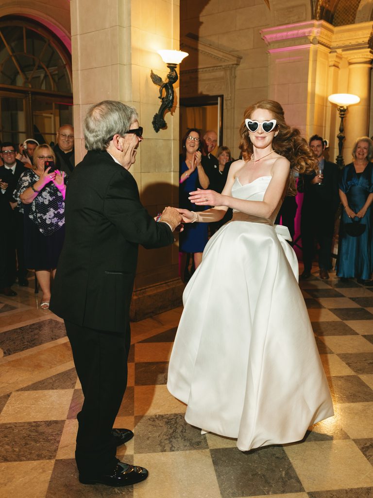Bride in heart shaped sunglasses dancing with her grandfather during the reception