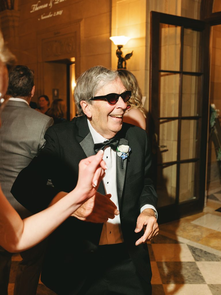 Smiling grandfather dancing with the bride during a luxury family celebration in warm indoor lighting